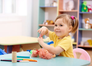 Happy preschool girl playing with toys in classroom
