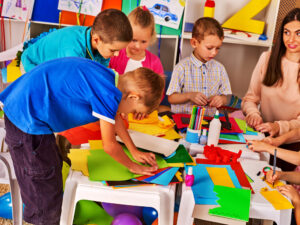 group of preschool children doing arts and crafts with colored paper and glue