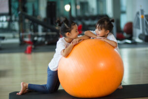 two children smiling and playing with large orange exercise ball