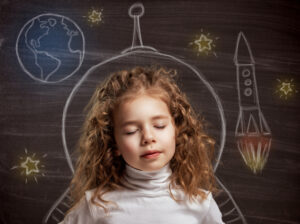 young girl imagining space adventure with chalk rocket drawing on blackboard