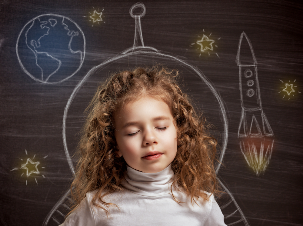 young girl imagining space adventure with chalk rocket drawing on blackboard