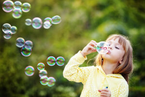 girl in yellow jacket blowing soap bubbles in park