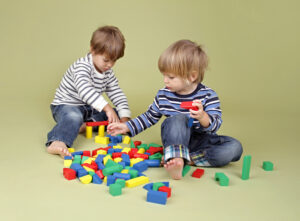 two toddlers building with red, blue, yellow, and green blocks