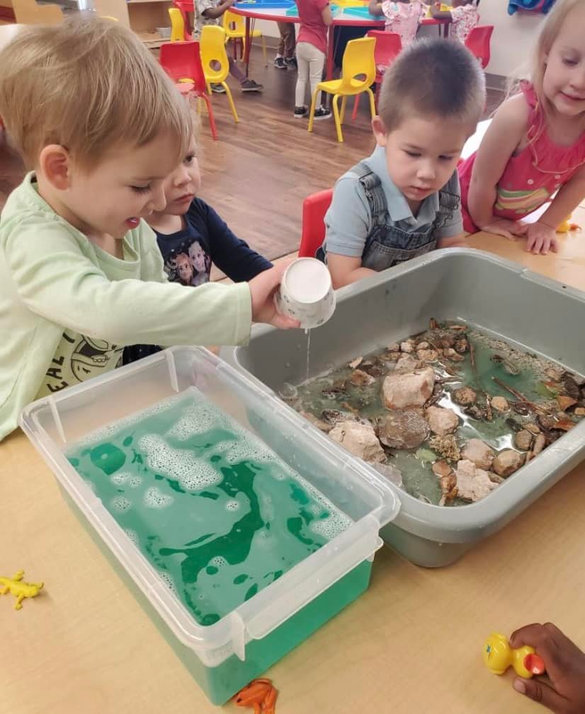 toddlers pouring water into sensory bins at preschool