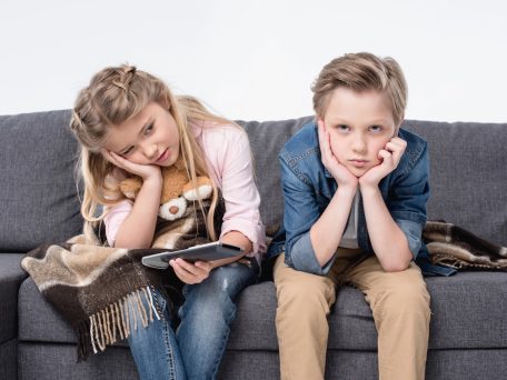 two children sitting on a couch looking bored