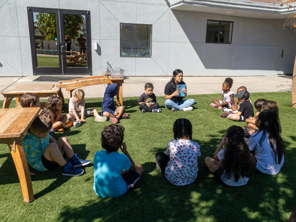 contact \ preschool children sitting on grass during outdoor circle time