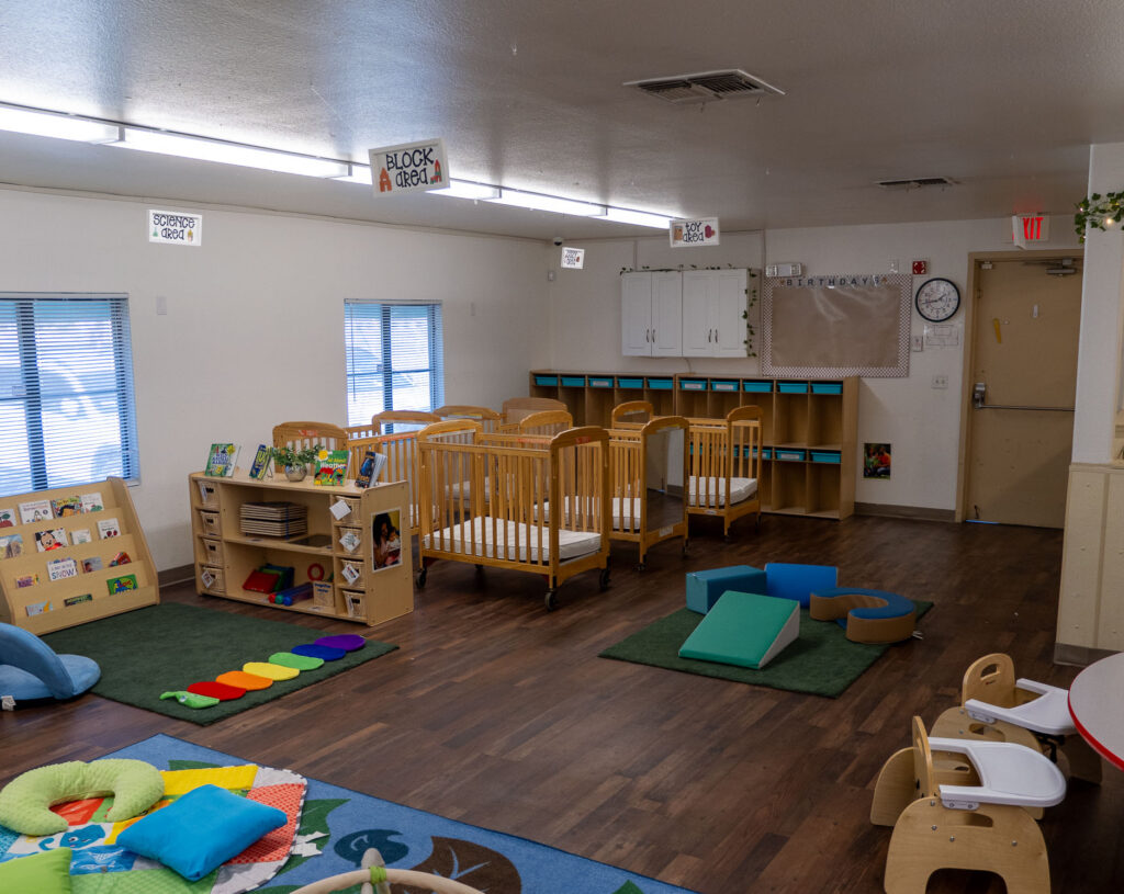 infant classroom with cribs, reading shelf, and play mats